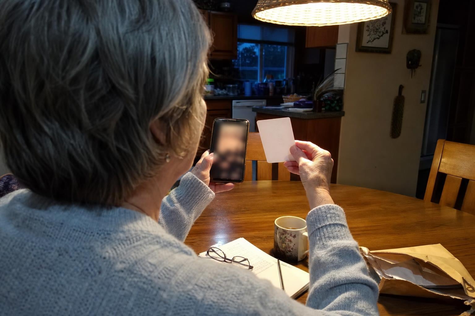 A woman comparing a restored photo on her phone against the original print, seen over her shoulder