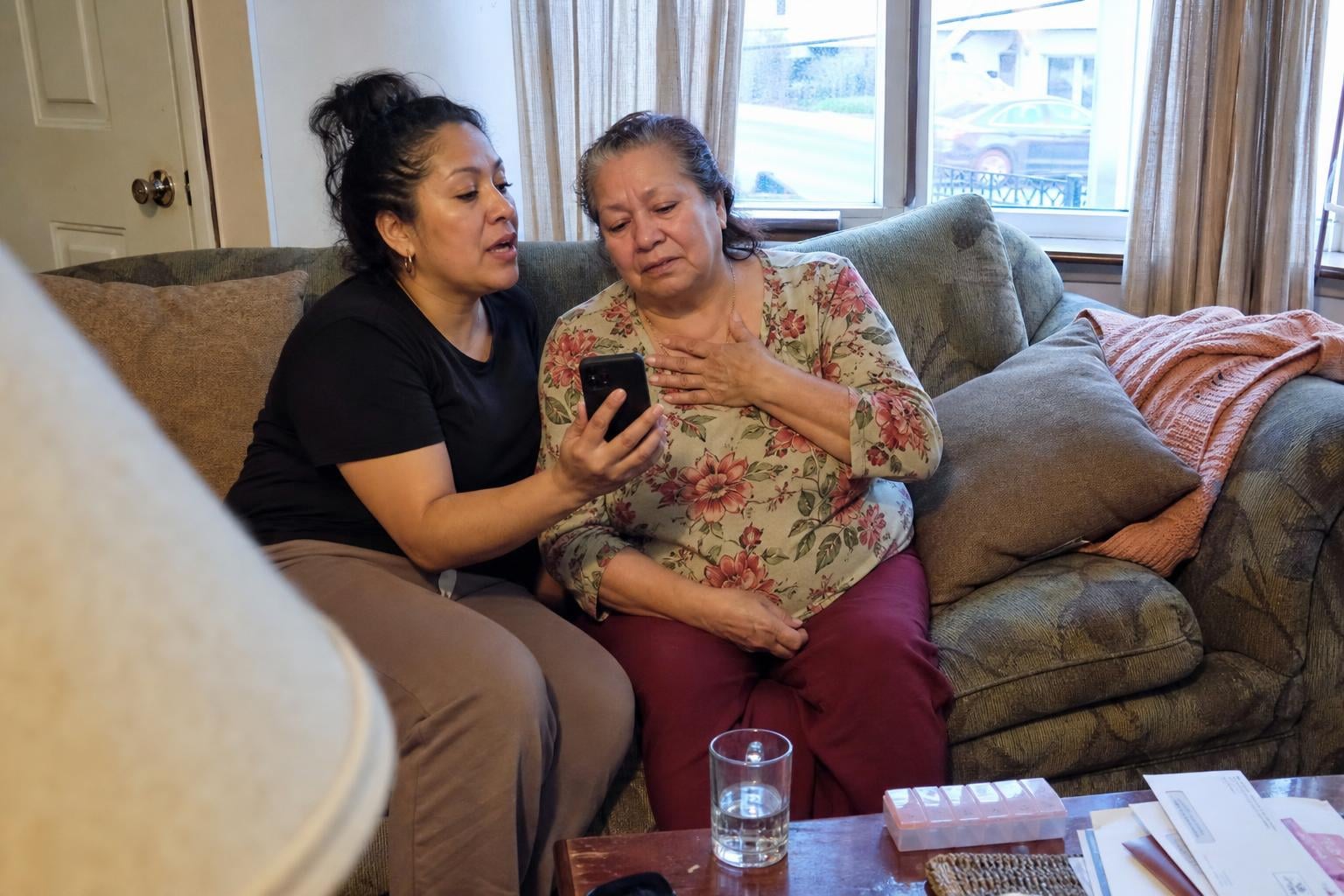 A daughter showing her mother a restored family photo on her phone as they sit together on the sofa