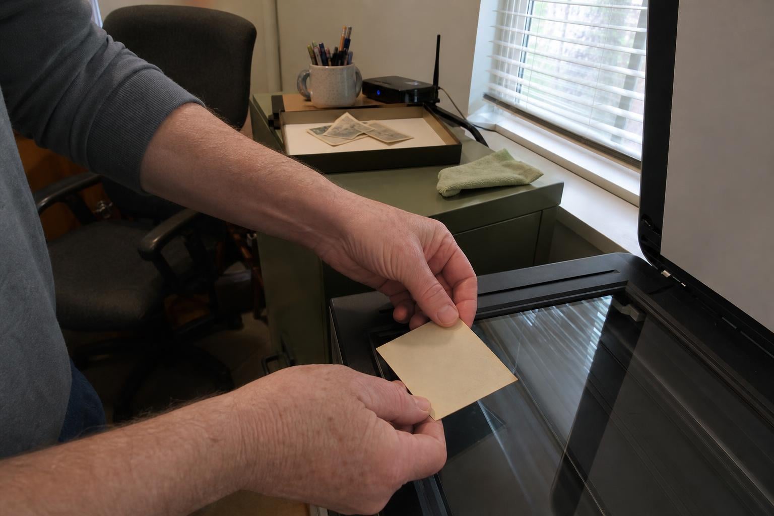 Hands lowering an old photograph face-down onto a flatbed scanner